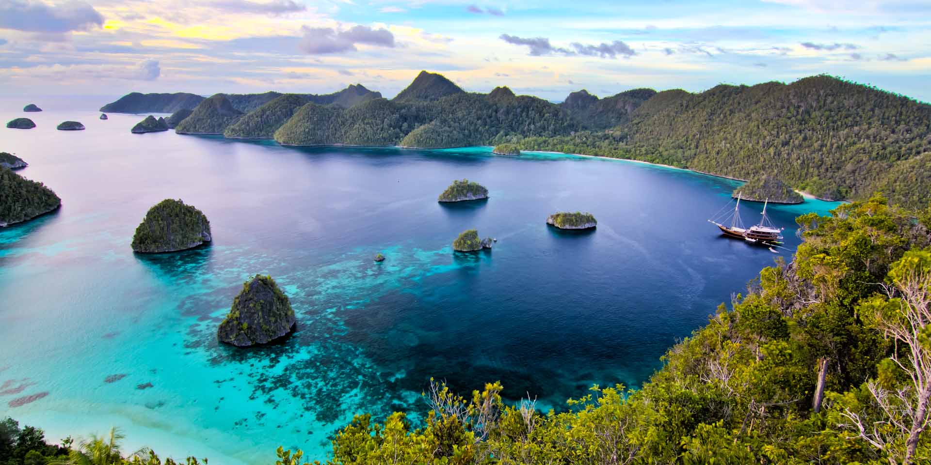 Dunia Baru sailing into a bay in Raja Ampat during sunset
