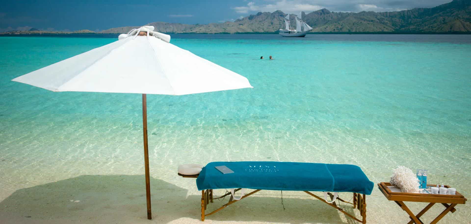 Massage table set-up on a white beach with a parasol and oils during Alexa's romantic adventure for a couple