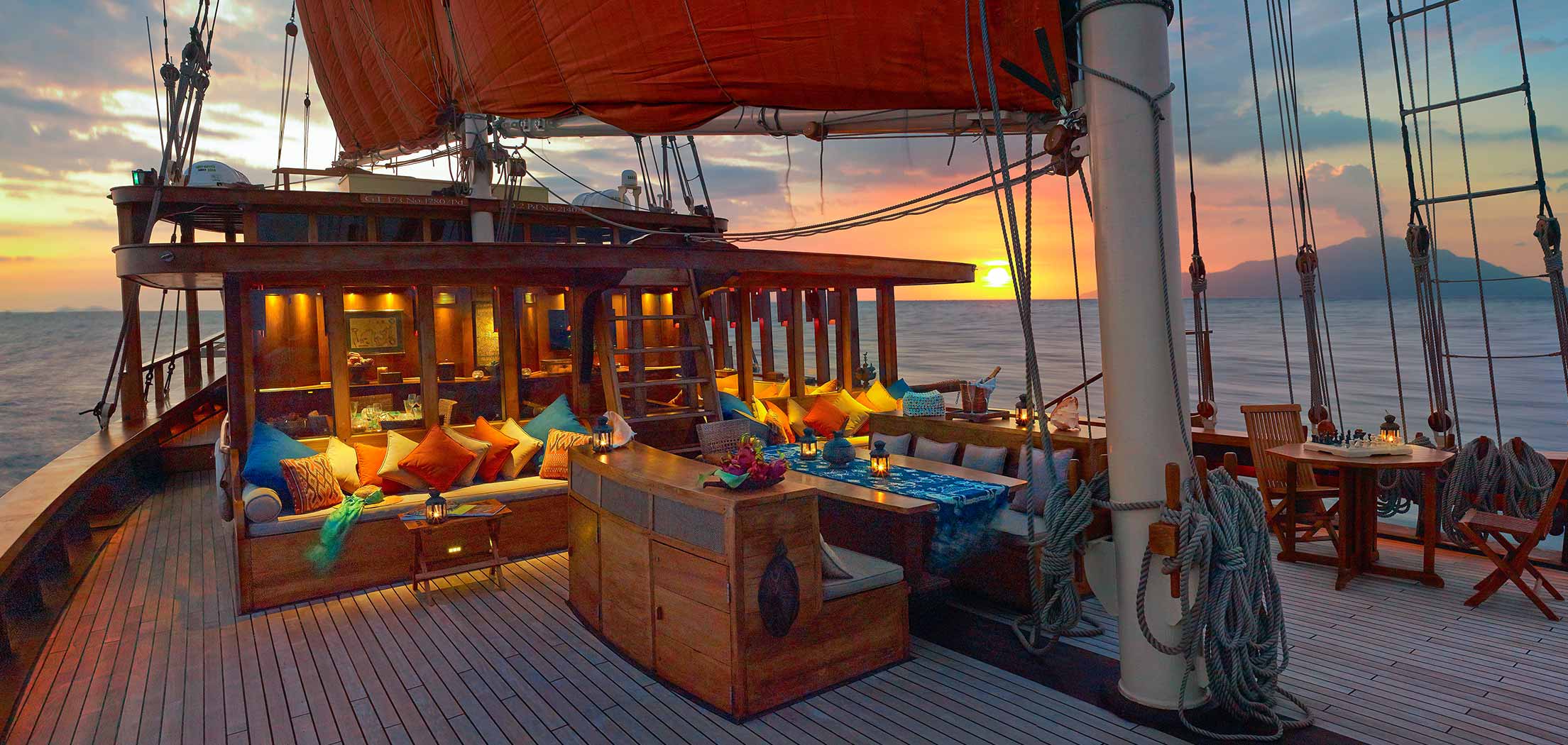 Outside dining area on deck of a luxury wooden Indonesian yacht for charter at sunset