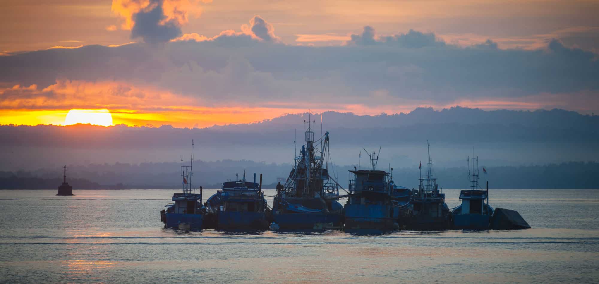 Small boats anchored at sunset in Sorong, a yacht charter gateway to Raja Ampat