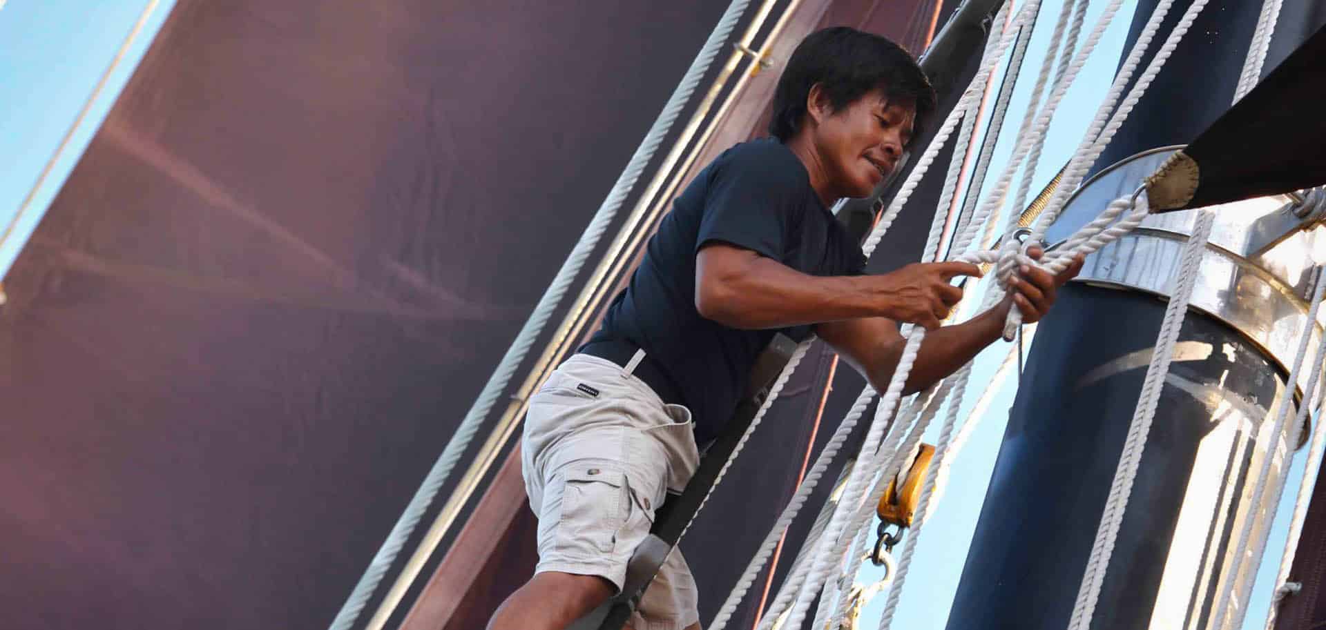 A crew member of Dunia Baru tightening a knot on the rope of a sail