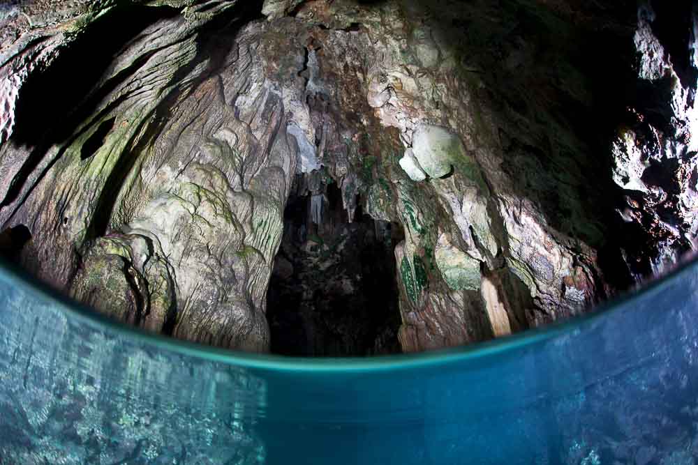 Half underwater view of the turquoise ocean in a rocky cave near Misool