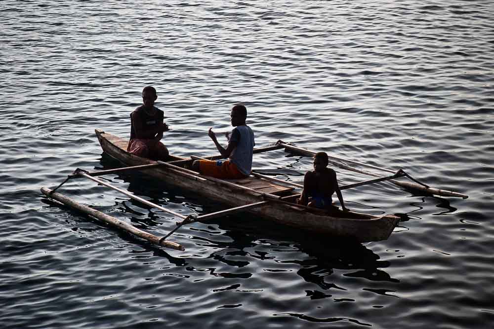 Three native Indonesian men of Boo islands swimming in a traditional long wooden fishing boat