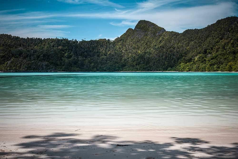 View from the white sand beach of Wayag on the turquoise waters and mountainous island covered with forest