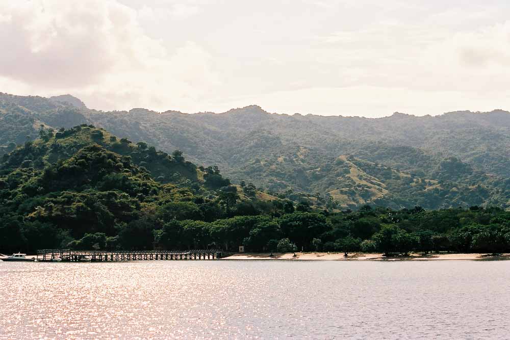 View on the shore with a pier and a wide beach of Komodo Island, with green hills in the background