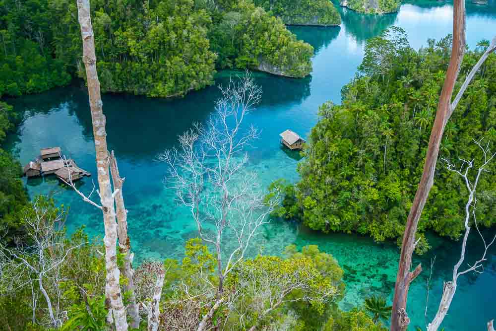 Aerial view on wooden huts built on turquoise waters of Penemu, in between small green islands