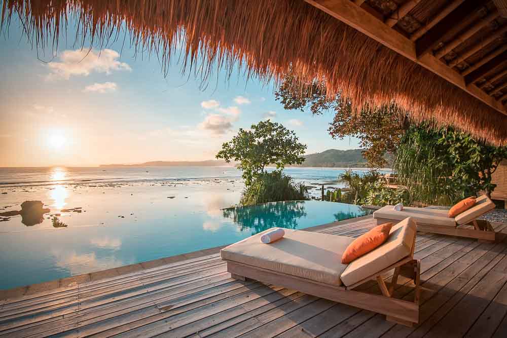 Two sun beds prepared for charter clients by infinity pool in Haweri at Nihi luxury resort, at sunset