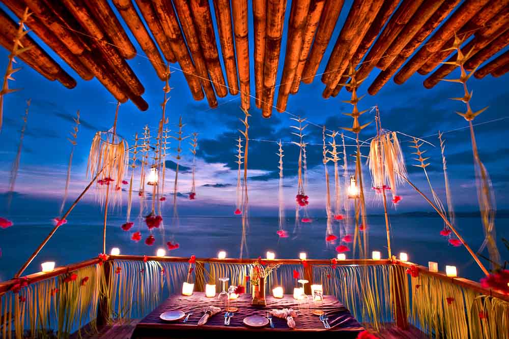 Dinner table set at dusk for two clients by the sea, with romantic decorations at Nihi luxury resort