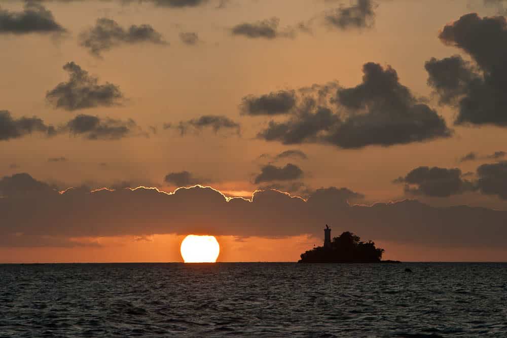 View from Sorong's harbor to the sea and a small island with a sun setting behind the clouds