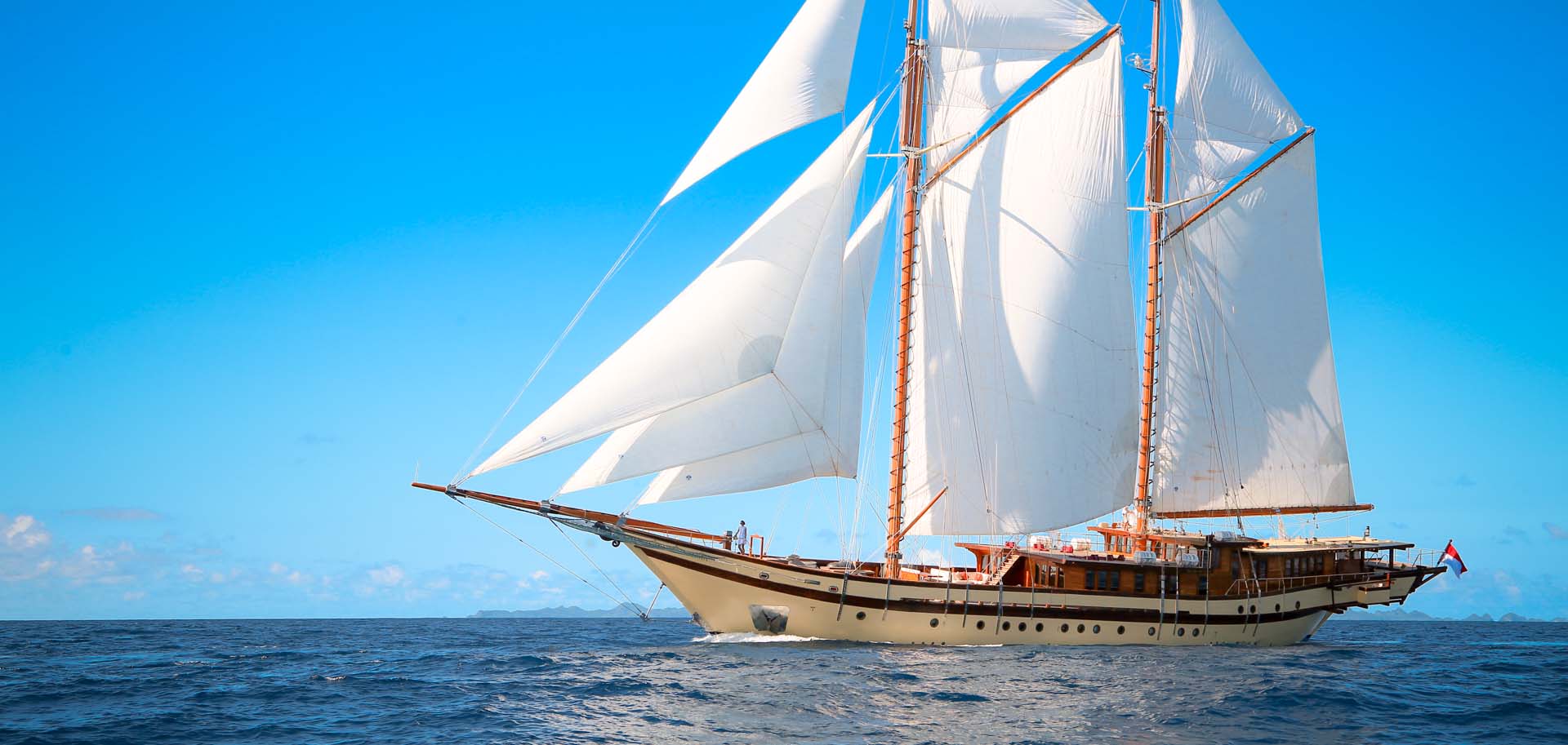 Side view of the charter superyacht Lamima with her sails up, cruising through blue waters of Indonesia